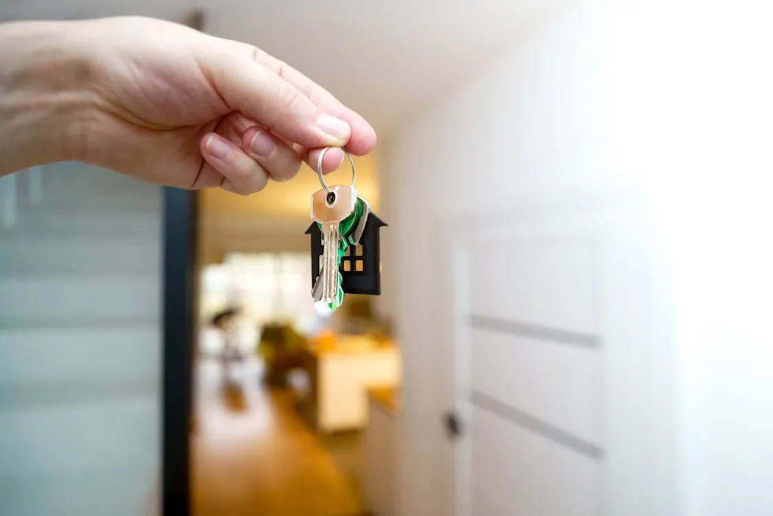 A hand offering house keys with a small wooden home keychain — the moment a lease takes effect in Davao